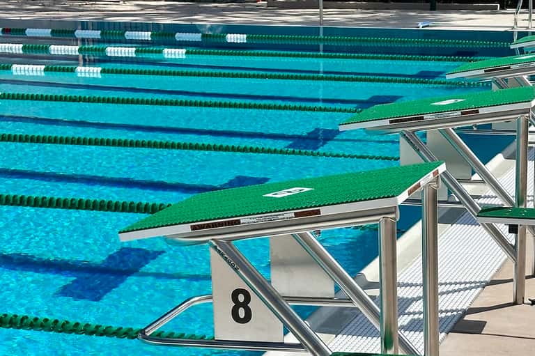 Olympic-style swimming pool with multiple lanes, lane dividers, and diving board platform