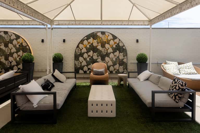 Rooftop lounge with white tent canopy, modular seating, decorative wall panels, and green turf