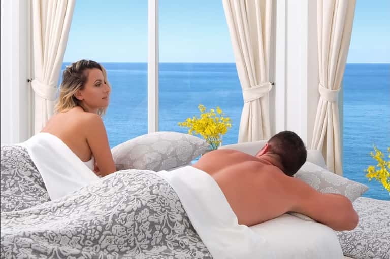 Couple relaxing on bed with ocean seascape view through large windows with flowing curtains