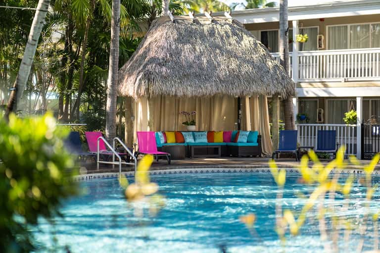 Thatched-roof poolside cabana with colorful cushions beside a resort pool and tropical landscaping