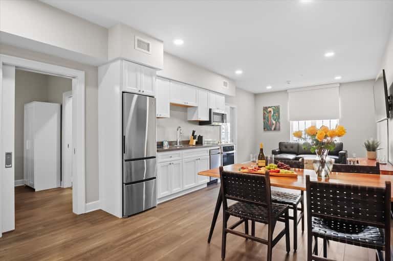 Bright modern apartment kitchen with white cabinetry, stainless steel appliances, and dining table
