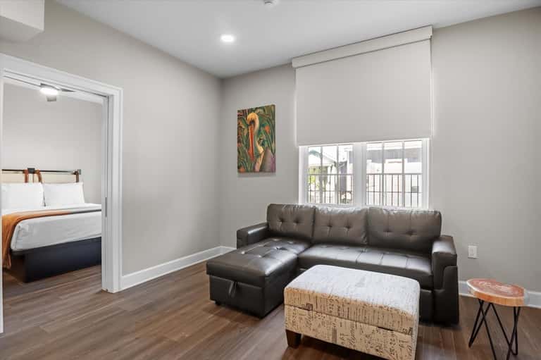 Modern resort bungalow interior with bedroom, black leather sofa, hardwood floors, and glass door
