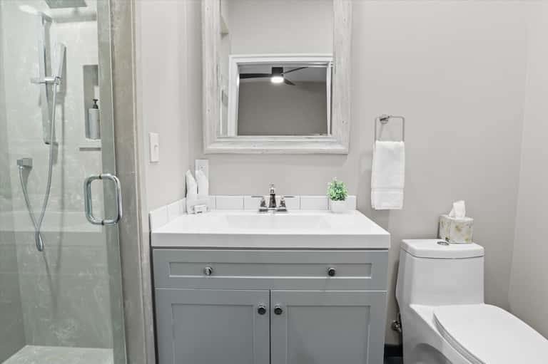 Clean modern bathroom with gray vanity, white sink, shower, and framed mirror