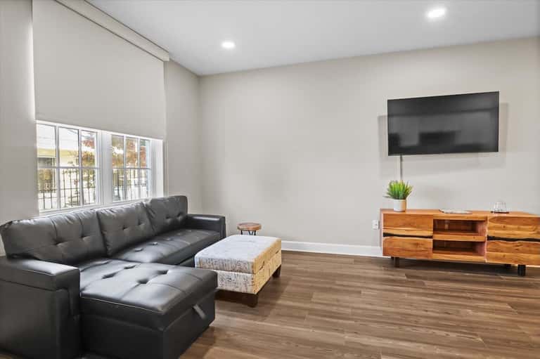 Contemporary living room with black leather sectional, wooden TV stand, and waterfront windows