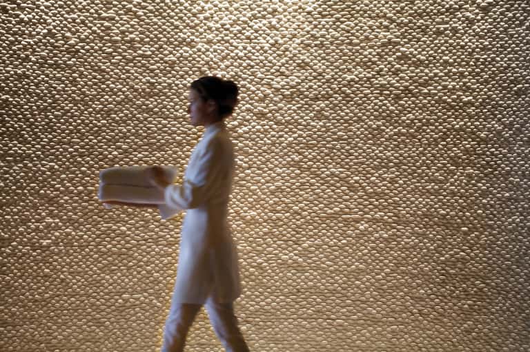 Spa attendant walking past textured beige wall in wellness facility wearing white robe