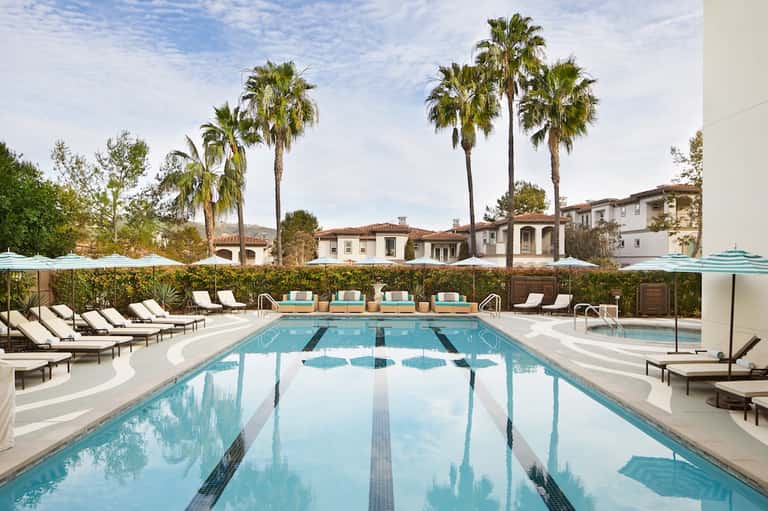 Olympic-style lap pool with lounge chairs, umbrellas, and palm-lined resort grounds