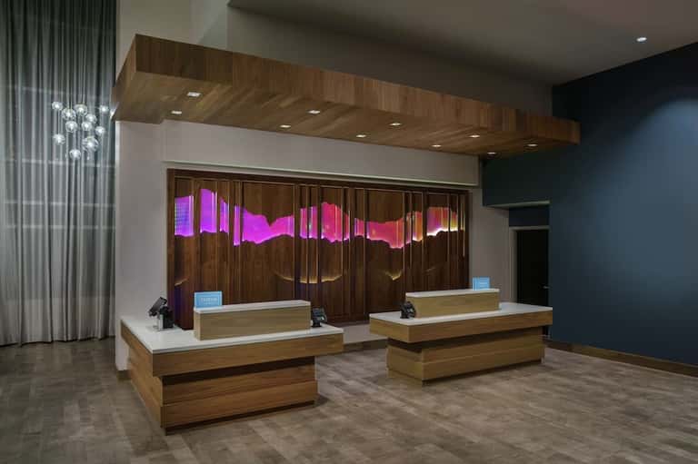 Modern hotel reception desk with dual white counters, wooden soffit, pink neon signage, and ambient lighting