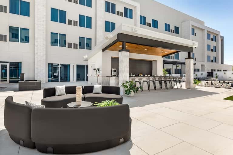 Modern hotel courtyard with curved black seating pod, white shade structure, and residential building facade