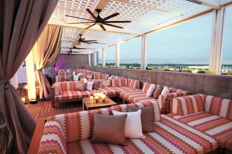 Modern rooftop lounge with pink striped seating, ceiling fans, floor-to-ceiling windows with valley views