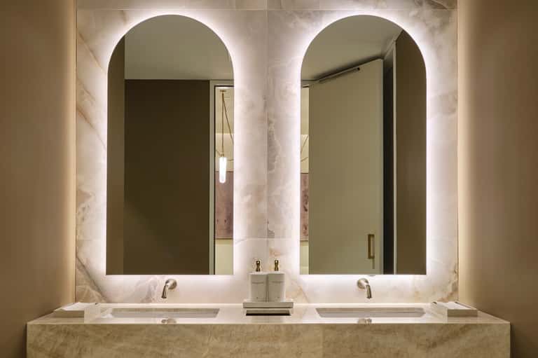 Luxury bathroom with dual vessel sinks, marble countertop, and two arched illuminated mirrors