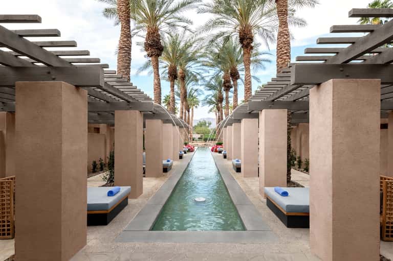 Luxurious spa corridor with slotted pergolas, palm trees, and narrow reflecting pool with lounge beds