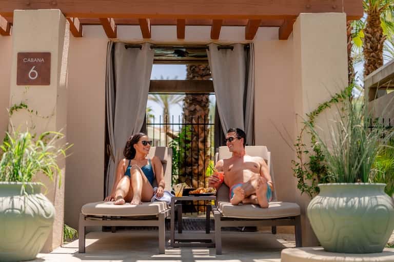 Couple relaxing in private cabana lounge chairs with ocean view and potted plants