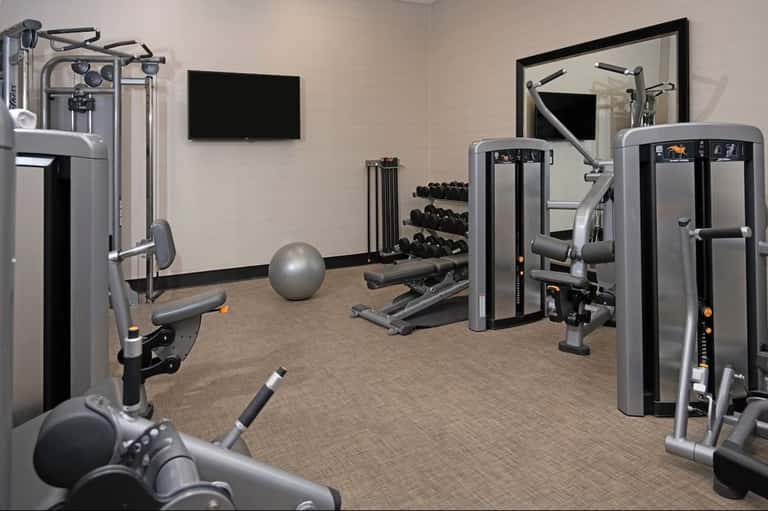 Modern fitness center with cardio equipment, weights, and flat-screen TV