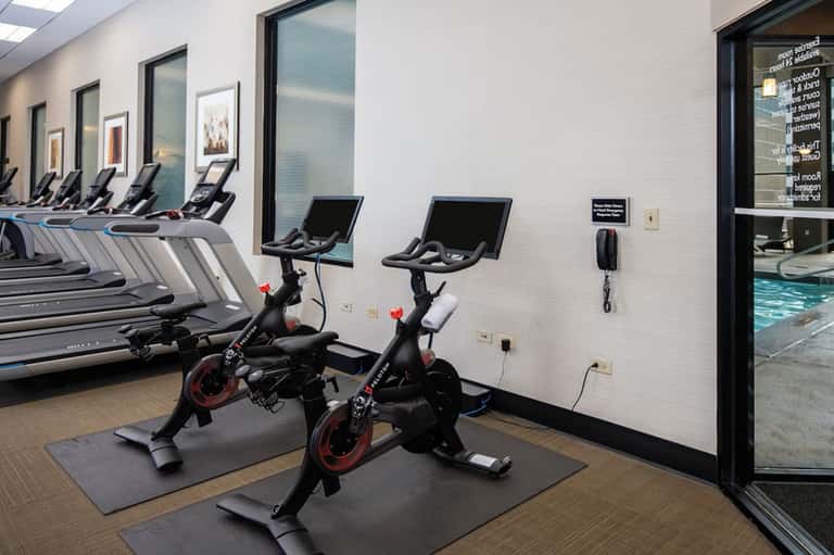 Fitness center with spinning bikes, treadmills, and large windows overlooking pool area