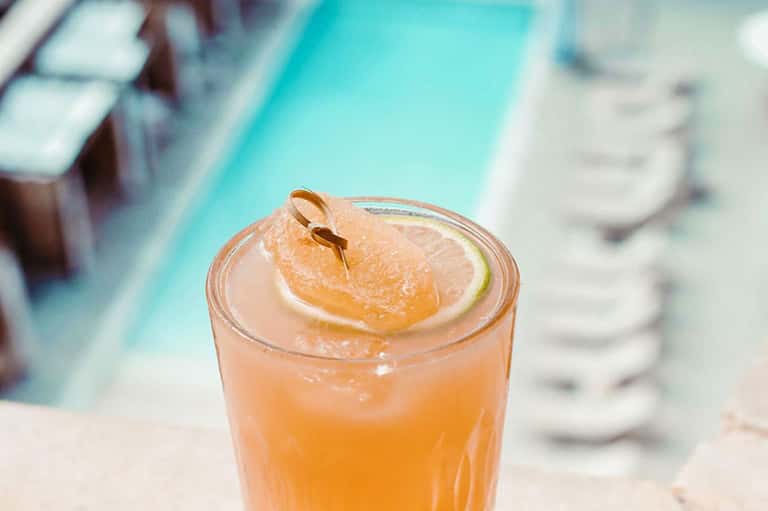 Peachy cocktail with citrus slice and metal pick garnish by pool