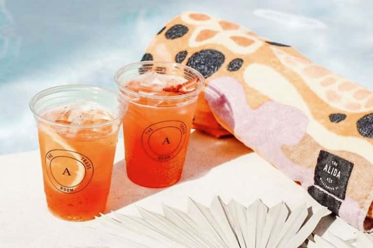 Two orange beverages with ice at beachside resort, branded cups beside patterned towel