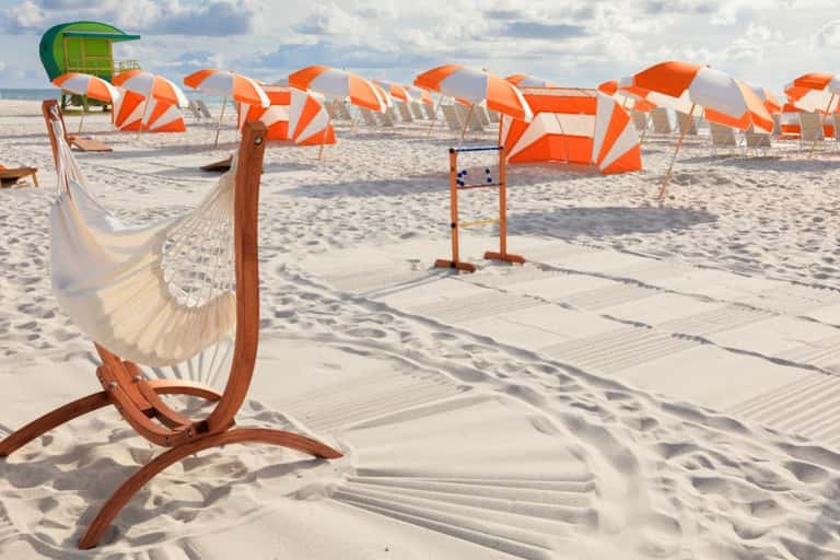 Sandy beach with white hammock and orange-white beach umbrellas lined along shore