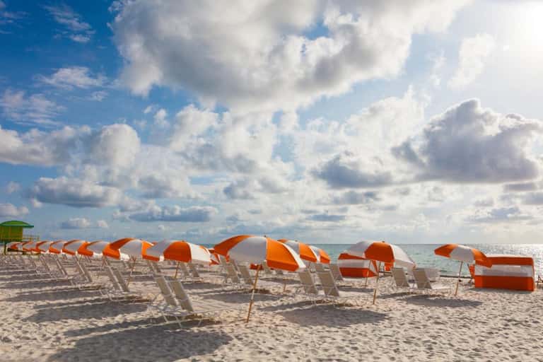 Rows of orange and white striped beach chairs arranged on sandy shore with ocean and cloudy sky
