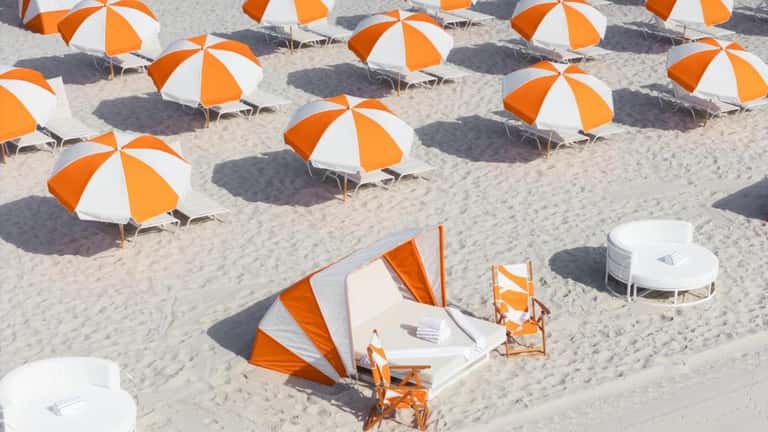 Beach amenities with rows of orange and white umbrellas and striped beach tents on sandy shore