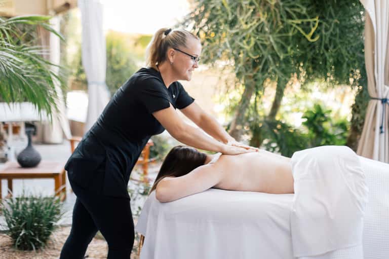 Outdoor spa massage treatment with therapist and client in garden setting with greenery
