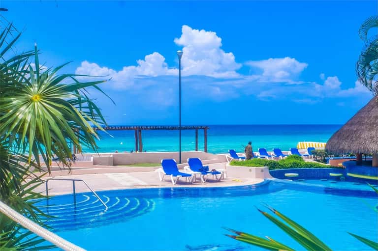 Turquoise infinity pool overlooking clear blue ocean with palm trees and tropical cabanas