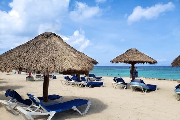 Beach scene with thatched-roof palapas, blue lounge chairs, and turquoise ocean water