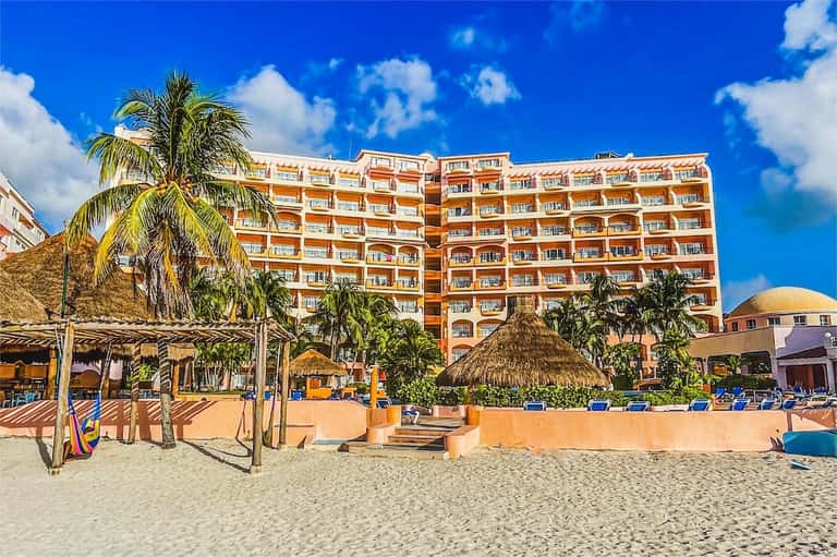 Orange resort building with thatched umbrellas and beach loungers on sandy beach