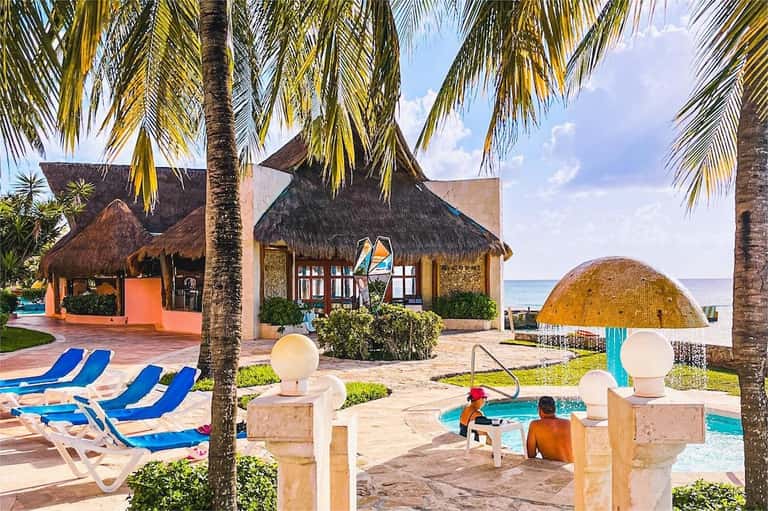 Beachfront resort with tiki-roofed bungalows, lounge chairs, and turquoise water