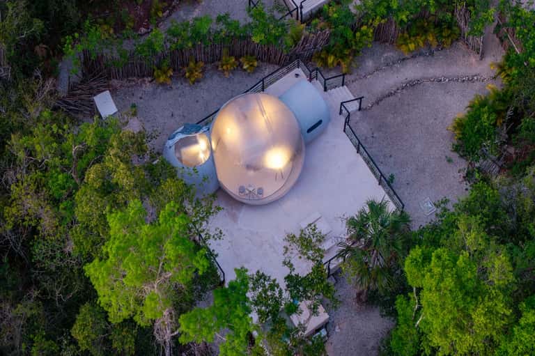 Aerial view of illuminated geodesic dome structure surrounded by native vegetation and sandy pathways