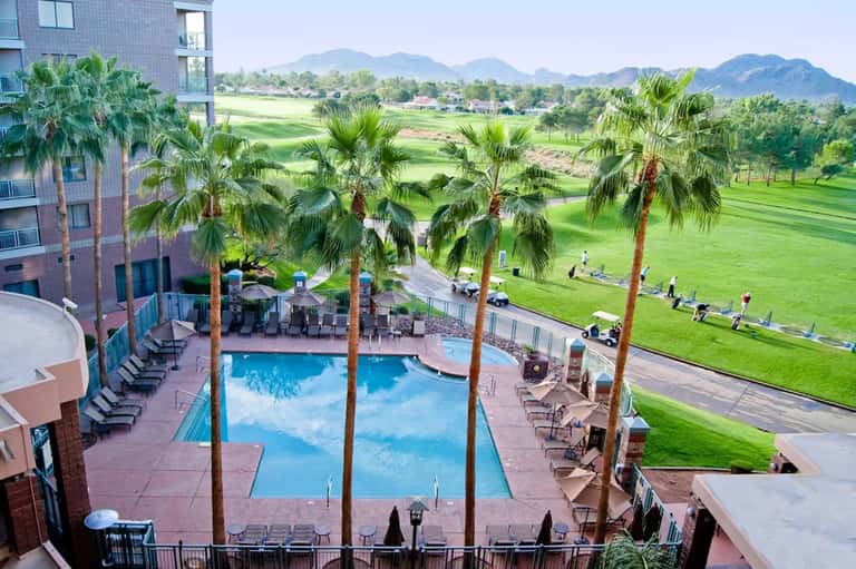 Resort pool with palm trees overlooking golf course and mountains in background
