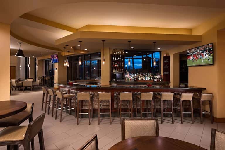 Upscale hotel bar and lounge with long counter, seating, pendant lighting, and evening views
