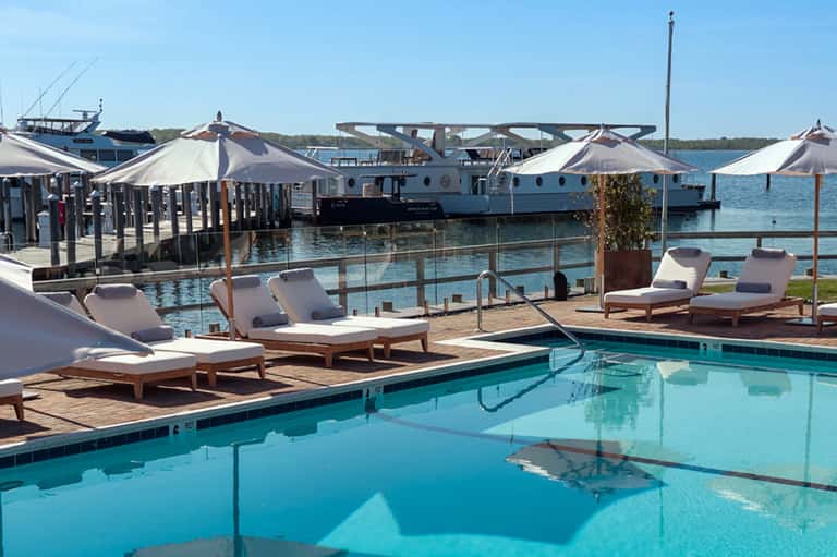 Waterfront resort pool deck with lounge chairs, umbrellas, and boats docked in turquoise water