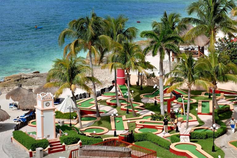Beachfront mini golf course with palm trees, clock tower, and turquoise ocean water view