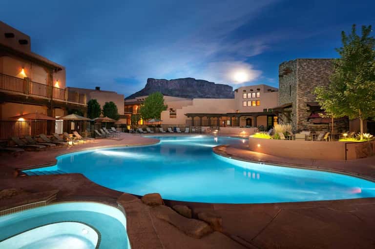 Illuminated resort pool with southwestern architecture and mountain backdrop at dusk