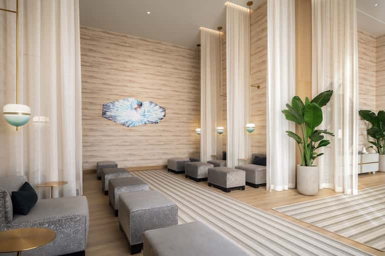 Spa relaxation area with wooden walls, tall sheer curtains, natural light, and lounge seating