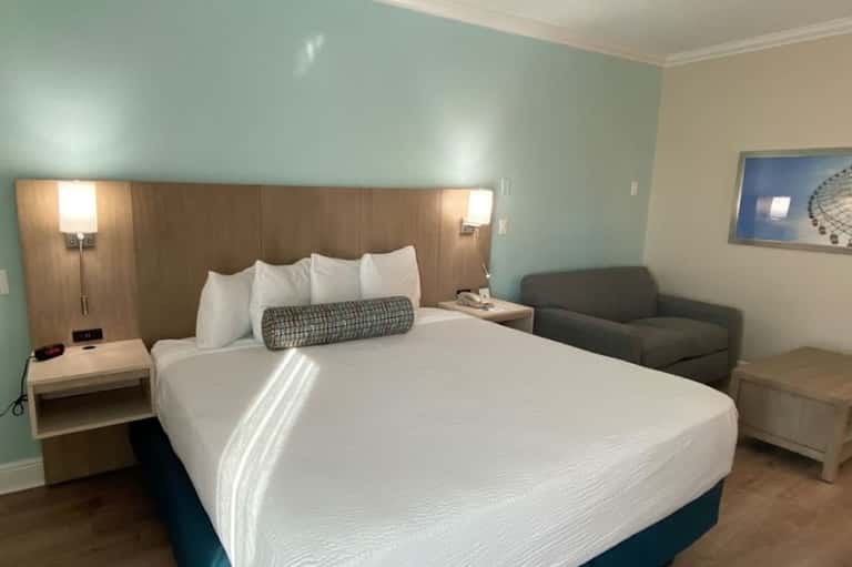 Modern hotel room with queen bed, mint green accent wall, wood headboard with reading lights, and armchair.
