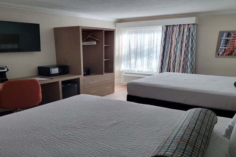 Hotel guest room with two queen beds, desk, TV, windows with curtains, and wood cabinetry