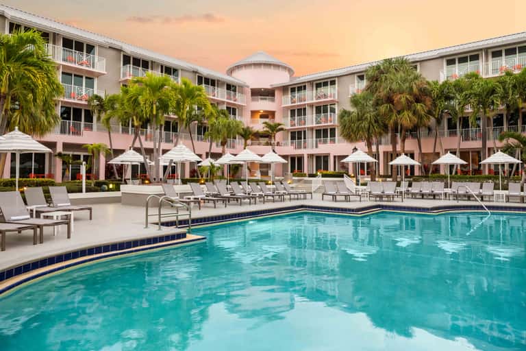 Pink beachfront resort at dusk with illuminated pool, lounge chairs, and umbrella seating