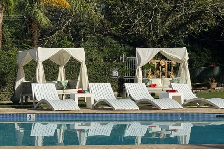 Poolside cabanas with white curtains, lounge chairs, and spa treatment beds near swimming pool