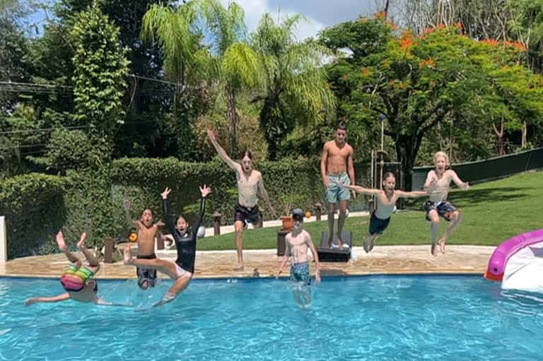 Children and adults jumping into bright blue pool surrounded by green lawn