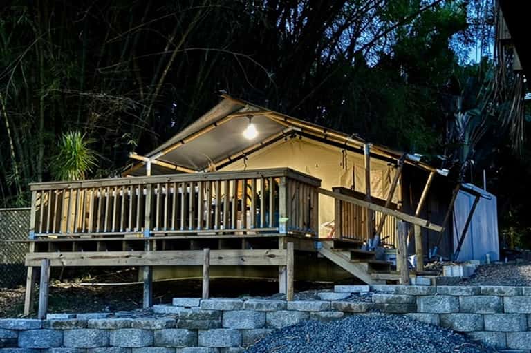 Illuminated glamping tent on elevated deck with tropical surroundings