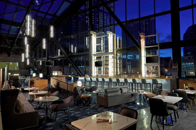 Contemporary rooftop bar with glass ceiling, city skyline views, bar seating, and dining tables