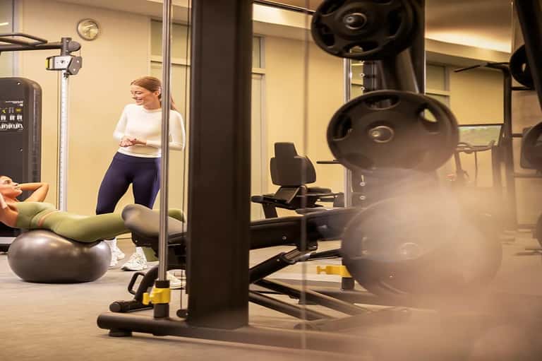 Female fitness instructor demonstrating exercise beside equipment in modern gym