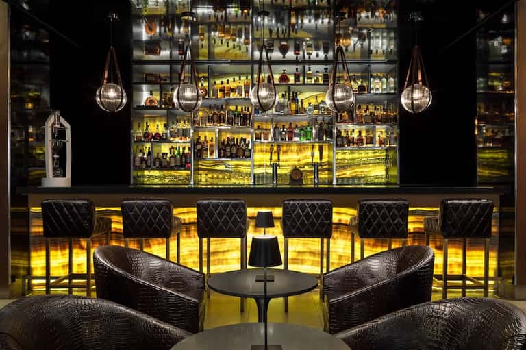 Upscale bar with illuminated shelving, hanging pendant lights, and quilted seating
