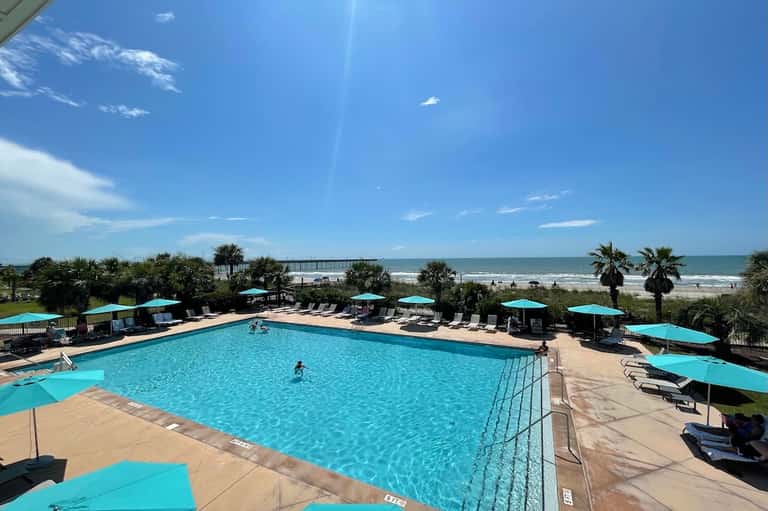 Oceanfront swimming pool with turquoise water, lounge chairs, umbrellas, and beach access