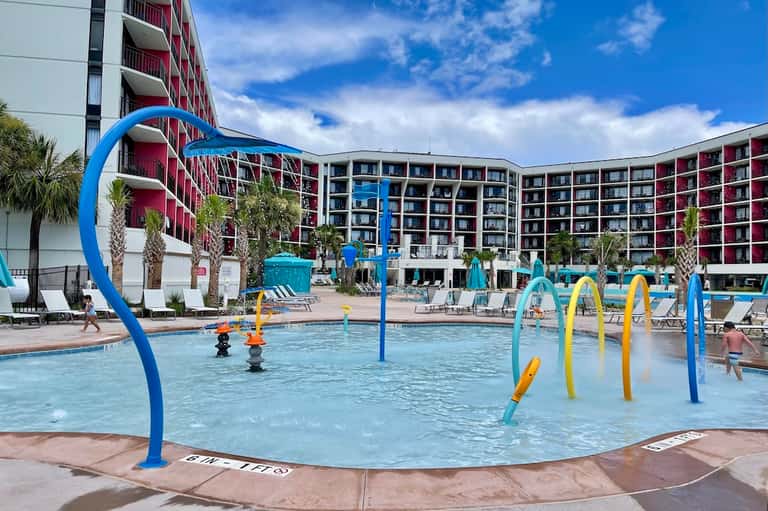 Family-friendly resort pool with colorful water play features and multi-story hotel building