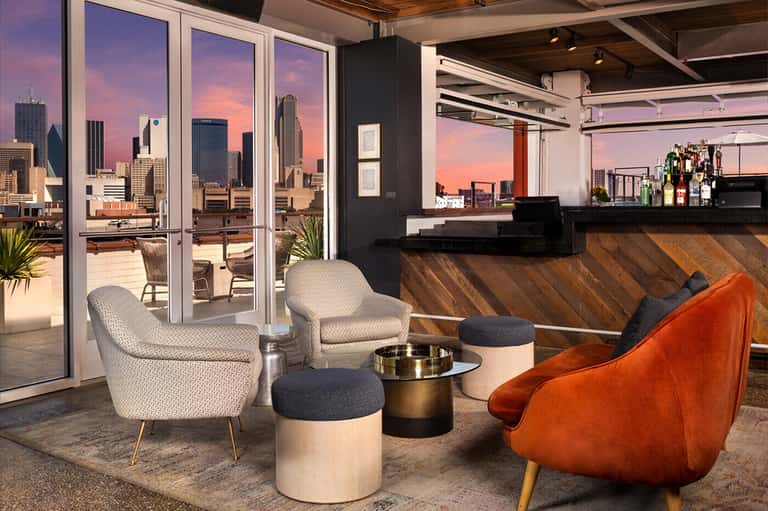Rooftop lounge with city skyline views, modern seating, and full bar at sunset