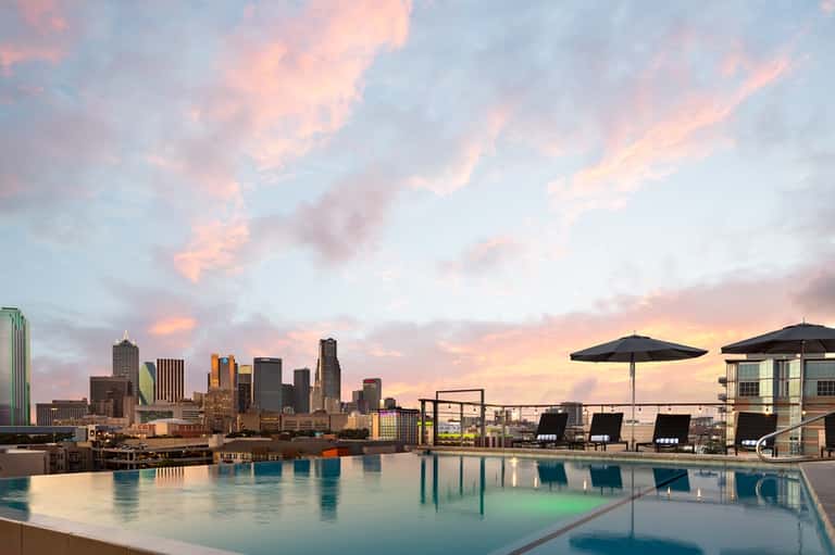 Rooftop infinity pool with city skyline view at dusk with umbrellas and lounge chairs