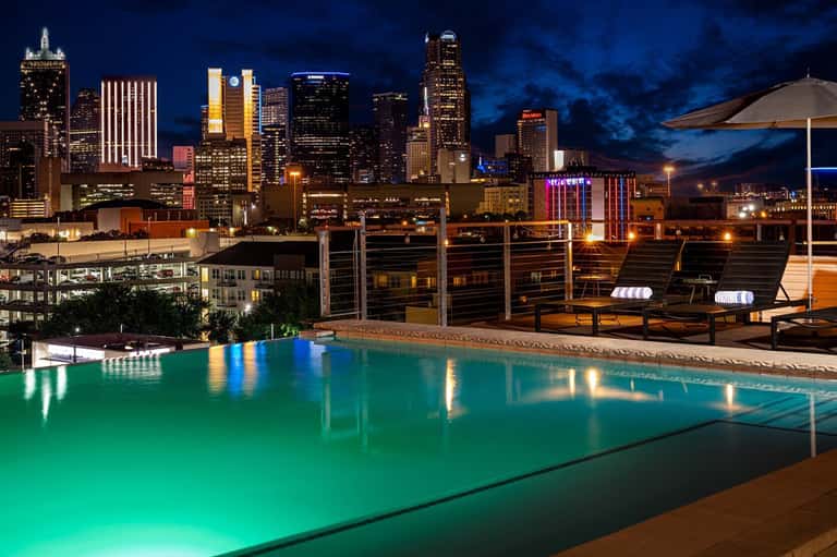 Illuminated rooftop pool with city skyline at night and modern lounge seating