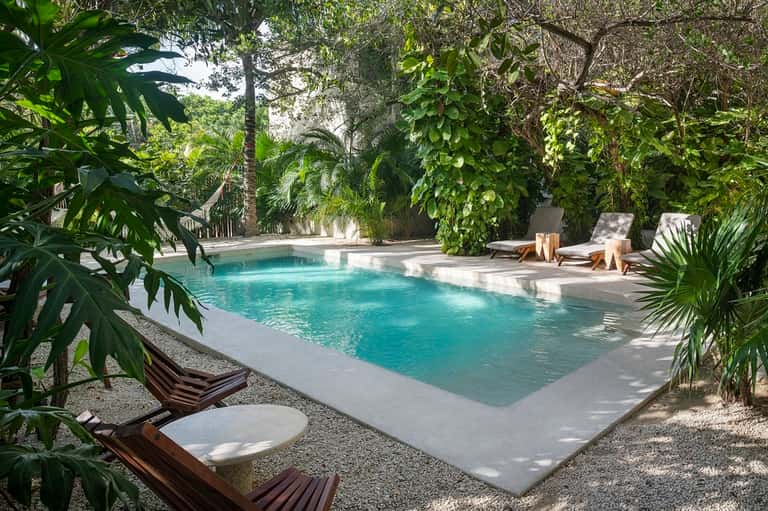 Tranquil resort pool surrounded by lush tropical vegetation and wooden lounge chairs with cushions